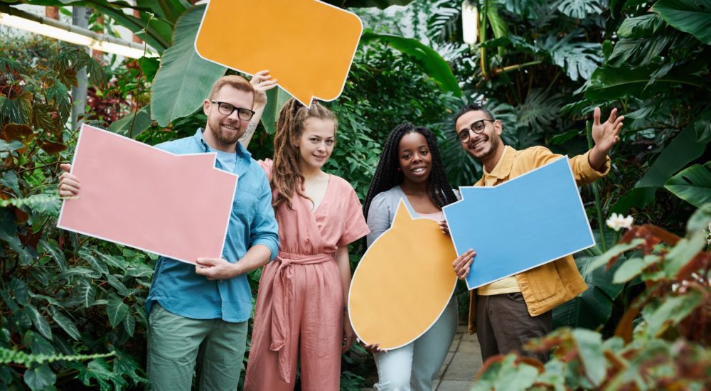 group of 4 people in a garden holding multi-colored thought bubble posters