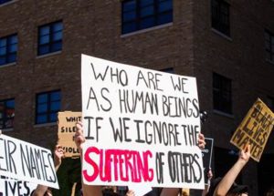 protest sign that reads, who are we as human beings if we ignore the suffering of others?