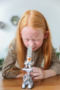 young girl using a microscope, a tool not available with at-home STEM learning