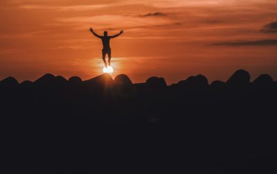 silhouette of person jumping with arms overhead against an orange sunset