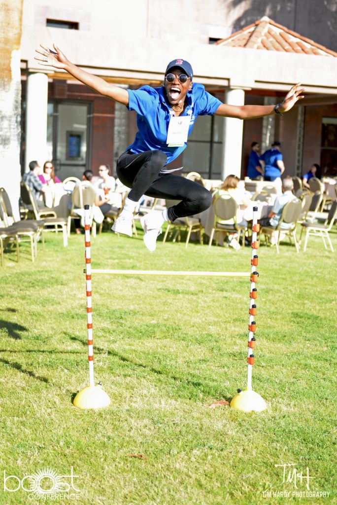 Smiling BOOSTer jumping over a limbo stick