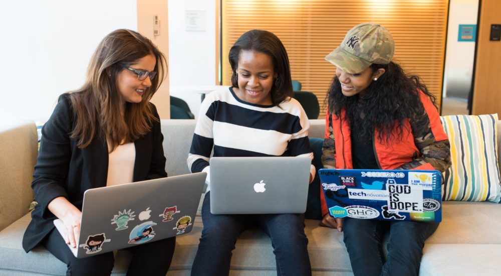 instructor and 2 young women smiling behind laptops