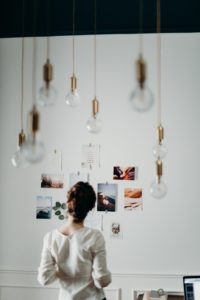 woman looking at images posted on a white wall with light bulbs hanging from the ceiling in the foreground
