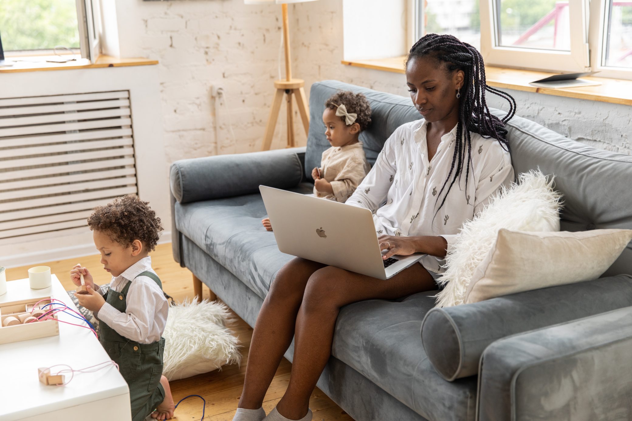 woman works on her laptop with two toddlers by her side