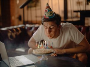 man blows out birthday candles alone in front of a computer