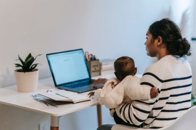working mom holds baby while writing on laptop