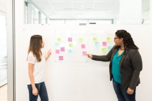 2 women lay out a communications plan with Post-It notes on the wall