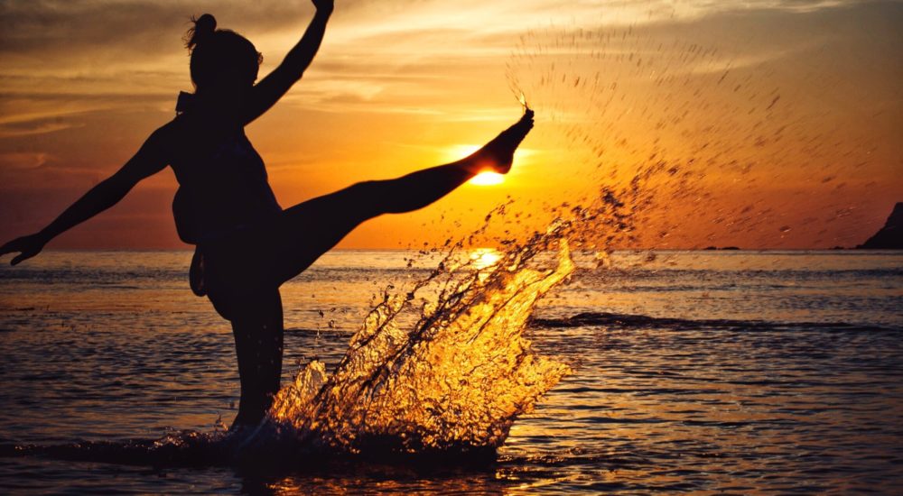 woman in silhouette kicking around in the ocean, making a splash