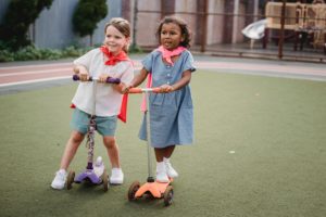 2 young girls ride scooters on a track building fitness through play