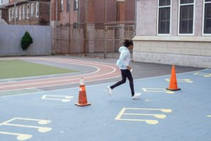 girl runs fitness drills around cones in the playground