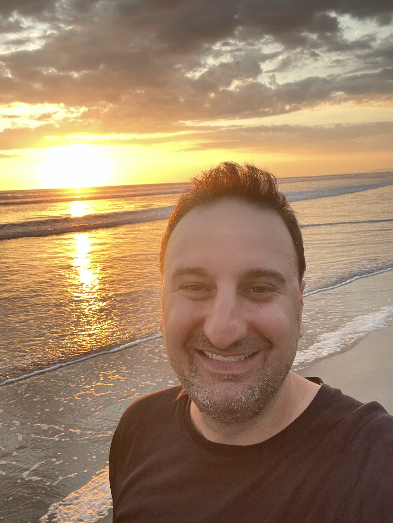 A photo of Joshua in front of a sunset over the ocean.