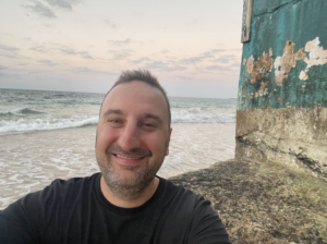 A photo of Joshua in front of the ocean.