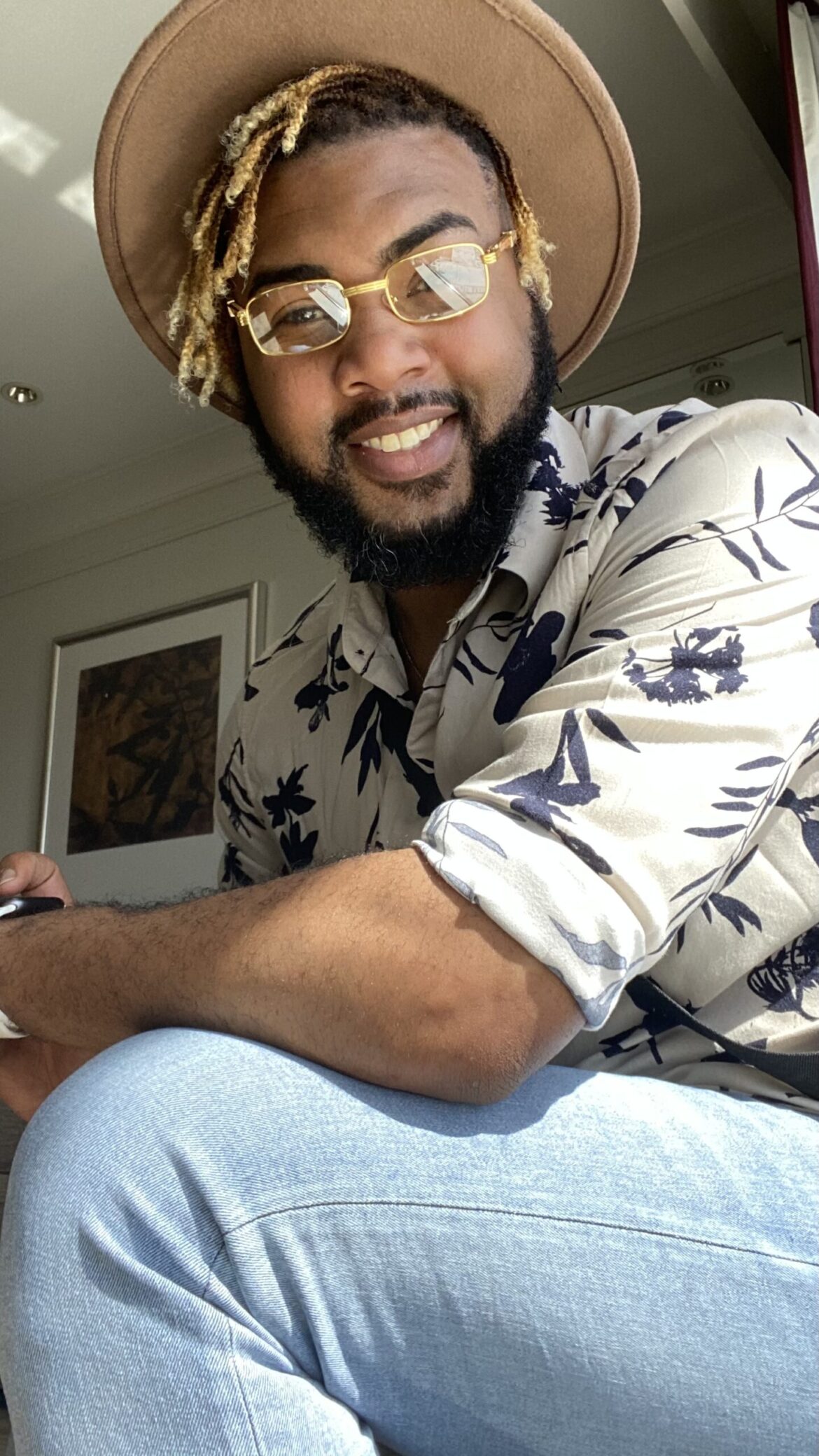 A photo of Richmond wearing blue jeans, a button up shirt, hat, and glasses.