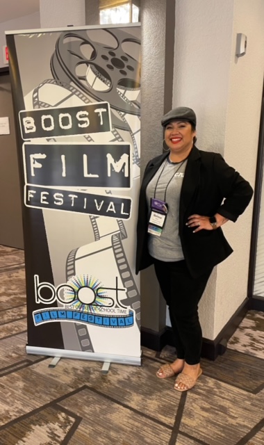 A photo of Melissa at BOOST Conference in front of the BOOST Film Festival banner.