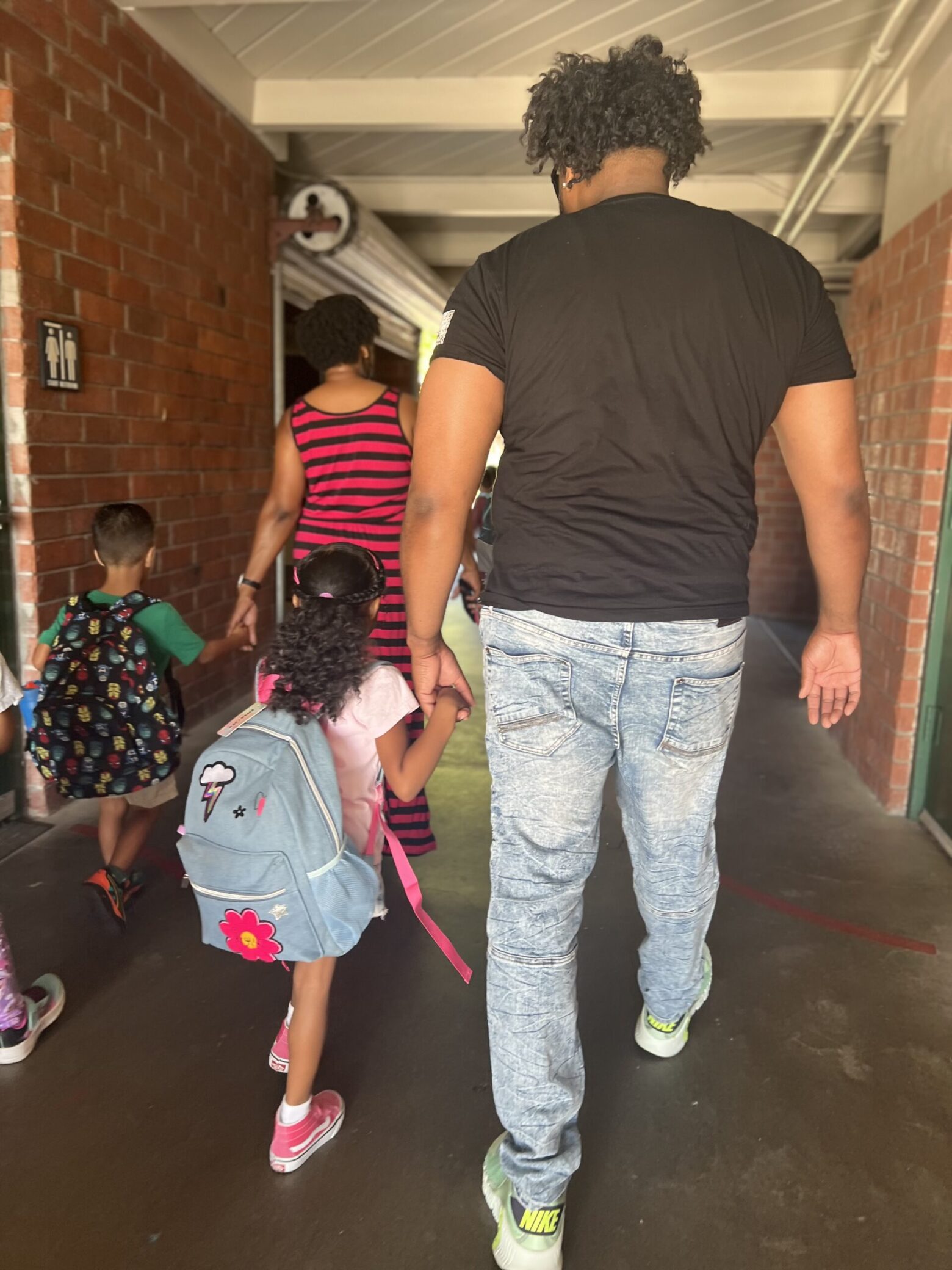 A photo of Nathan holding the hand of a young girl with her backpack.