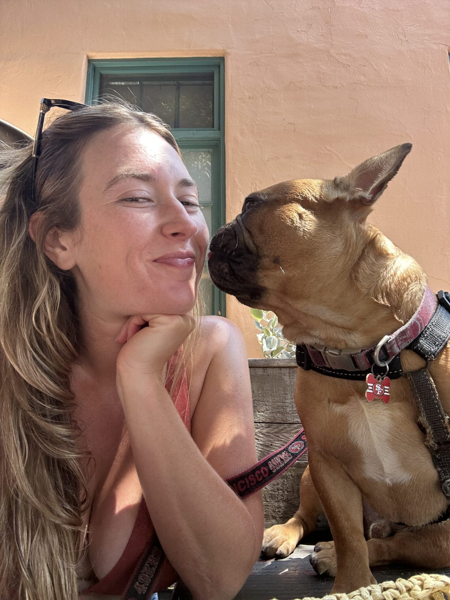 A photo of Nicolette and her dog, Warner. Warner is giving her a kiss on the cheek.