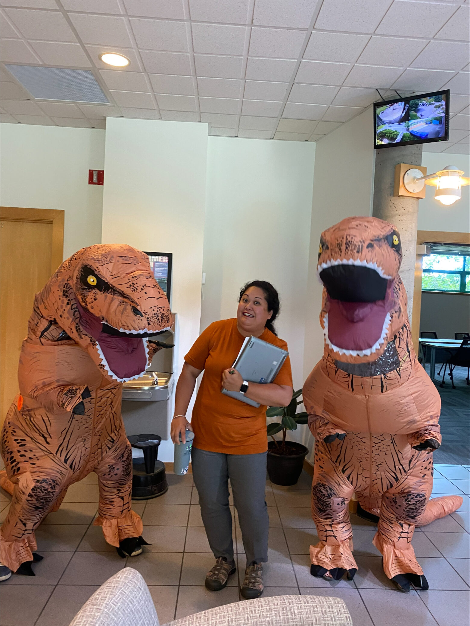 A photo of Sheryl in between two people dressed as dinosaurs.