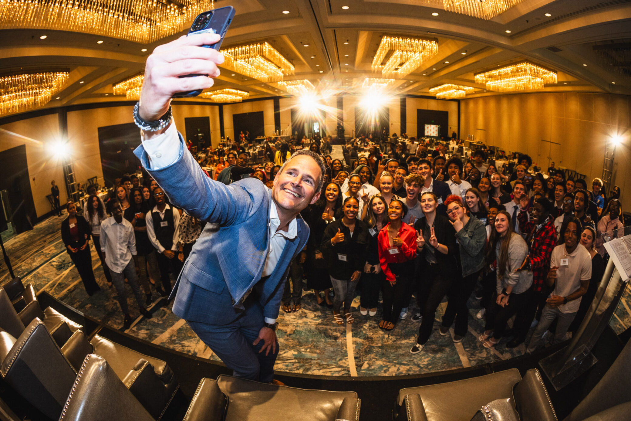 A photo of a man taking a selfie with a crowd behind him.