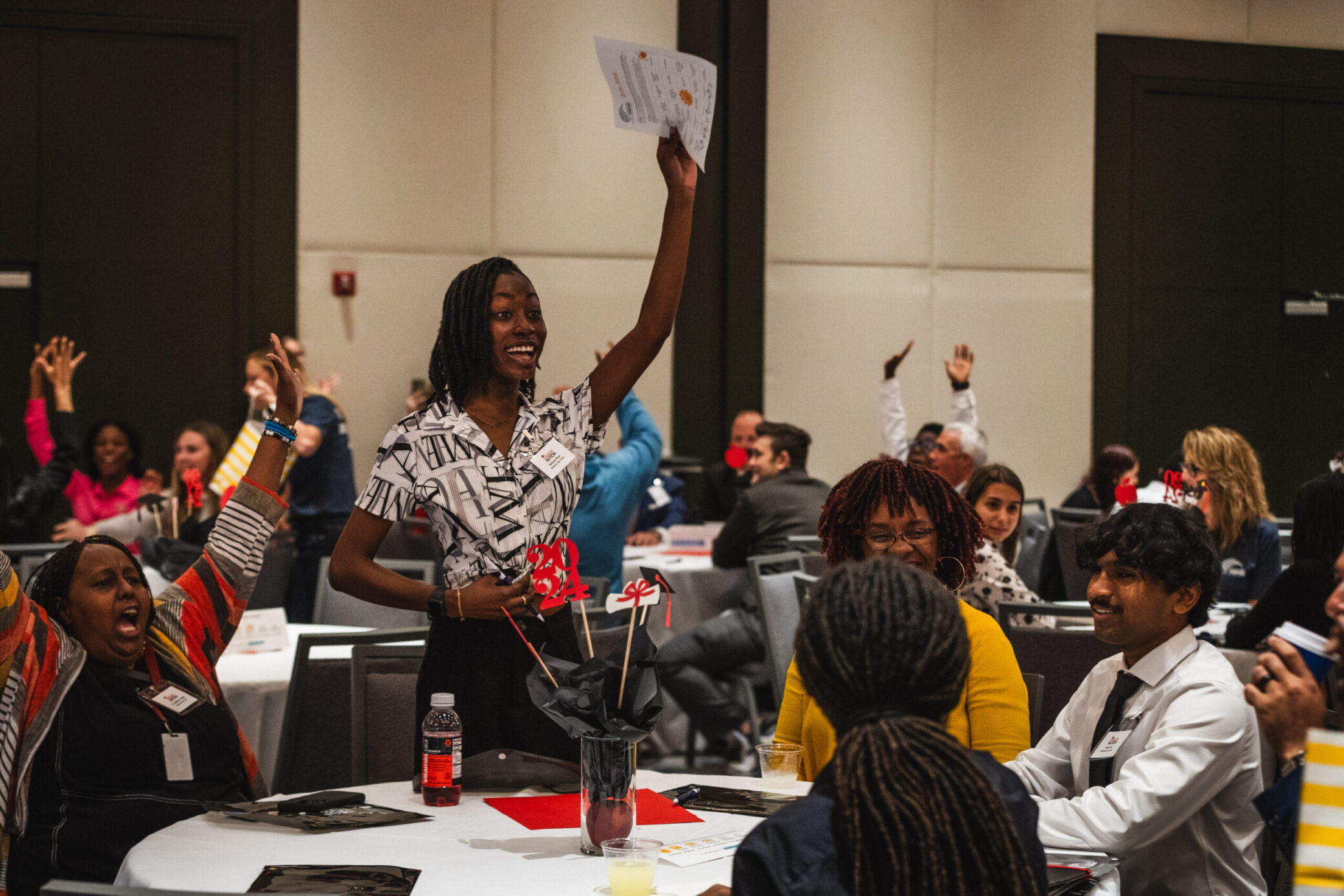 A photo of an adult standing with a piece of paper in the air. Other adults cheering around this person.